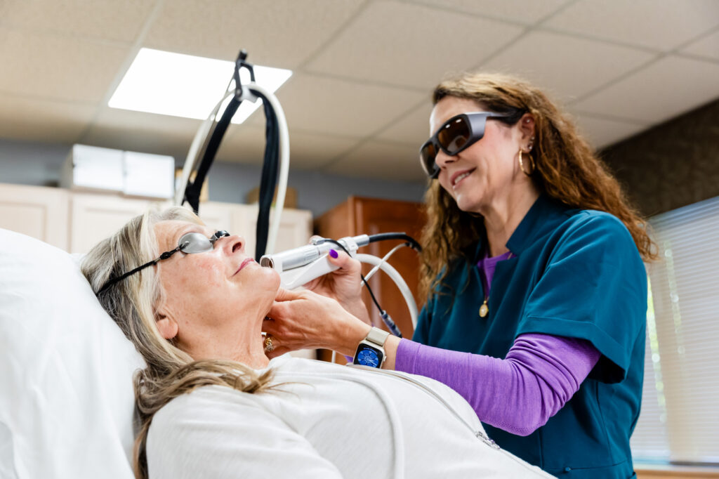 Provider wearing glasses places medical device on patient who is laying down wearing protective eye wear. This is treatment enhances skin care in Columbus, OH.